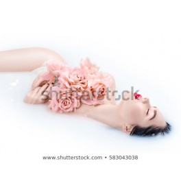 Beautiful Fashion model girl in milk bath, spa and skin care concept. Beauty young Woman with bright makeup and pink rose flowers relaxing in milk bath. Rejuvenation, skin pampering, treatment.